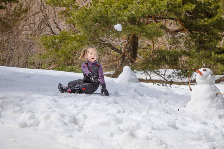 四岁的金发碧眼笑着的孩子在冬天的山上扔雪球，挨着雪人