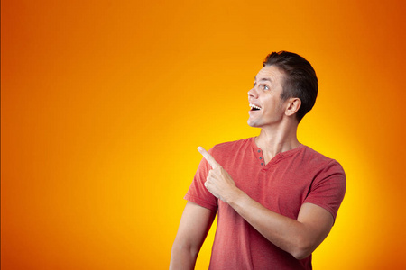 成年开朗的男人微笑着，用手指指着橙色的背景。 积极和成功的概念