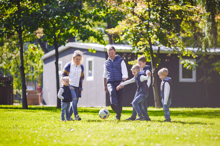 主题家庭户外活动..大而友好的高加索家庭，六个爸爸妈妈和四个孩子踢足球，在阳光明媚的日子里，带着球在草坪上奔跑，绿草地在房子附近