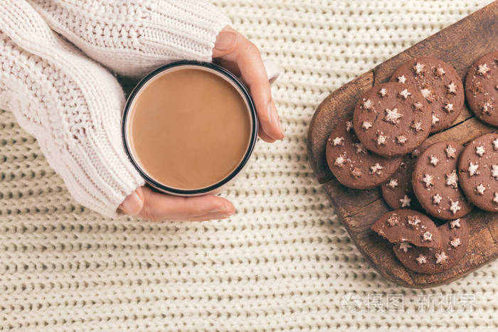 雌性手拿着一杯热可可巧克力饼干在木切割板上. 针织格子背景. 顶部视