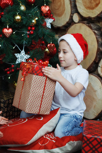 戴着圣诞帽的男孩坐着，手里拿着礼品盒，带着惊喜的喜悦。