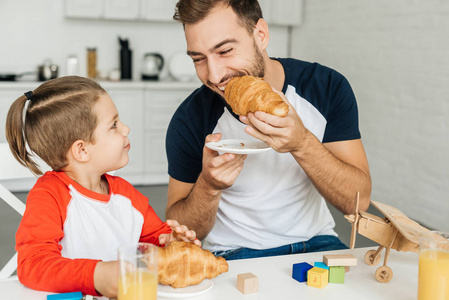 快乐的年轻父子在家一起吃羊角面包和橙汁早餐