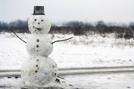 大有趣的传统原始微笑雪人与斗帽白色雪田冬季景观模糊的黑树和蓝天复制空间背景。 圣诞快乐，新年快乐。