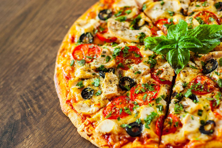 切片比萨饼与鸡肉，马扎雷拉奶酪，番茄橄榄。 木制背景意大利披萨