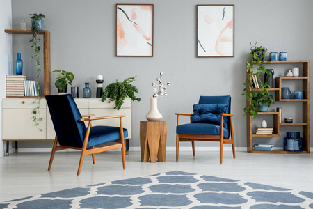 蓝色地毯在灰色客厅内部，海报和木桌之间的扶手椅。 真实照片