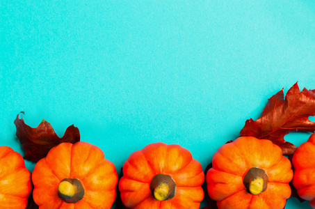 万圣节假期或秋季背景。 五个橙色南瓜，蓝色背景上有红色干燥的橡木叶。 从上面看。 复制文本空间。