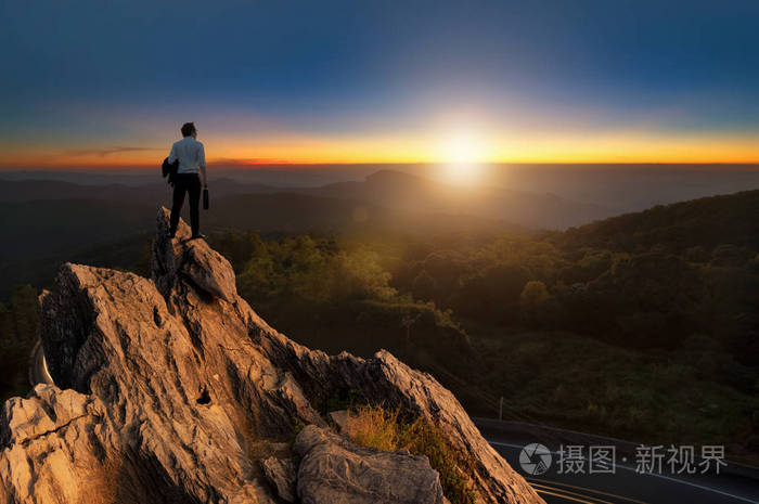 人穿着舒适的休闲西装外套,站在山顶上,手里拿着商务袋,期待着成功的