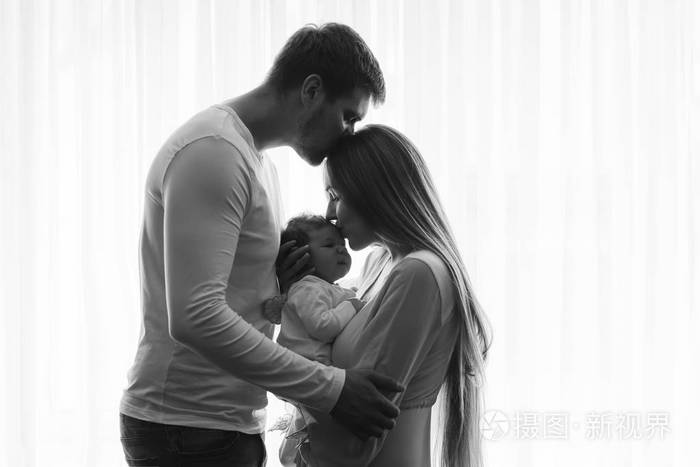 黑白相间的男人亲吻妻子时,她亲吻他们的小男孩在家门口的窗帘