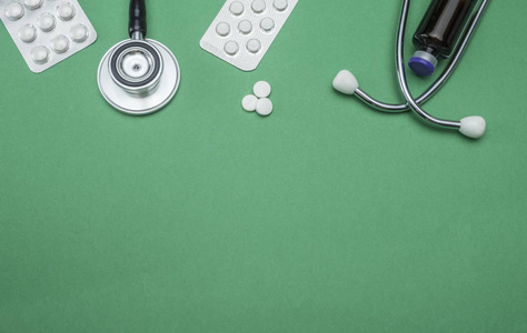 在绿色背景概念图像上分离的听诊器和药片