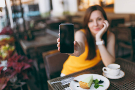 女人在户外街头咖啡店咖啡馆坐在桌子旁，手拿着一杯茶蛋糕，手拿着手机，空白的空屏幕在餐厅自由放松。 生活方式休息概念