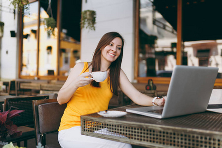 平静的女人在户外街头咖啡厅，坐在桌子上，工作在现代笔记本电脑，电脑，喝杯茶，在餐厅放松，在空闲时间。 移动办公自由职业概念