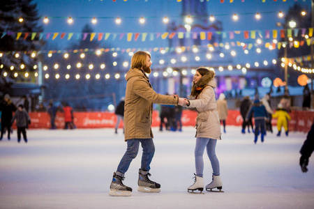 圣诞夜，一对金发长胡子的白种年轻情侣和一个美丽的女人在夜市广场的冰场上玩花样滑冰