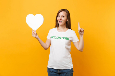 微笑的女人穿着白色T恤的肖像，上面写着绿色的标题，志愿者把白色的心隔在黄色的背景上。 自愿无偿援助慈善恩典工作概念