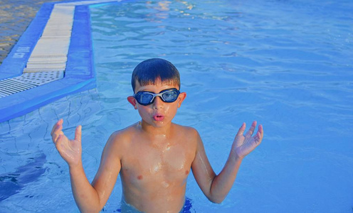 夏天在游泳池里戴着泳镜的可爱小男孩。 夏天和快乐的童年概念。 在明亮的蓝色水中复制空间。