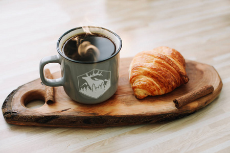 一杯热咖啡和羊角面包在木托盘上。早餐概念