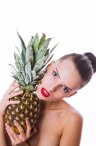 一个相当严肃的女人的肖像，她把菠萝靠近她的脸，贴在白色背景的室内