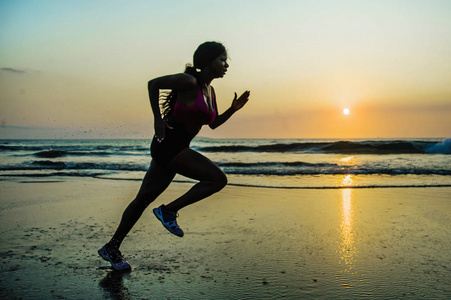 年轻快乐和有吸引力的非裔美国跑步妇女的剪影，她在美丽的海滩慢跑中进行健身冲刺锻炼，在健康的户外活动中享受日落