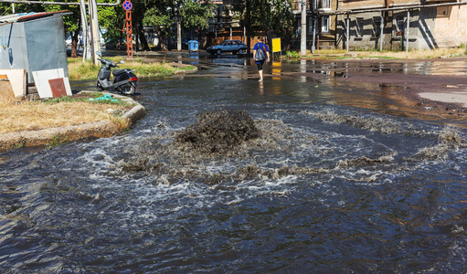 水从道路污水舱口流出。 污水的排水喷泉。 污水系统事故。 肮脏的污水在道路上流动喷泉。 从舱口流出的水