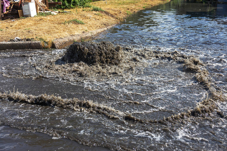 水从道路污水舱口流出。 污水的排水喷泉。 污水系统事故。 肮脏的污水在道路上流动喷泉。 从舱口流出的水