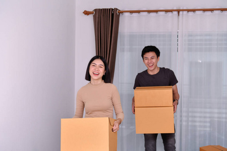 搬家概念。 亚洲年轻人正在携带他的物品。 年轻的亚洲女人把她们的东西放在一个纸箱里。 年轻人在新房子里很开心。