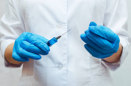 注射器与蓝色医疗药物在医生手中穿着医用长袍。