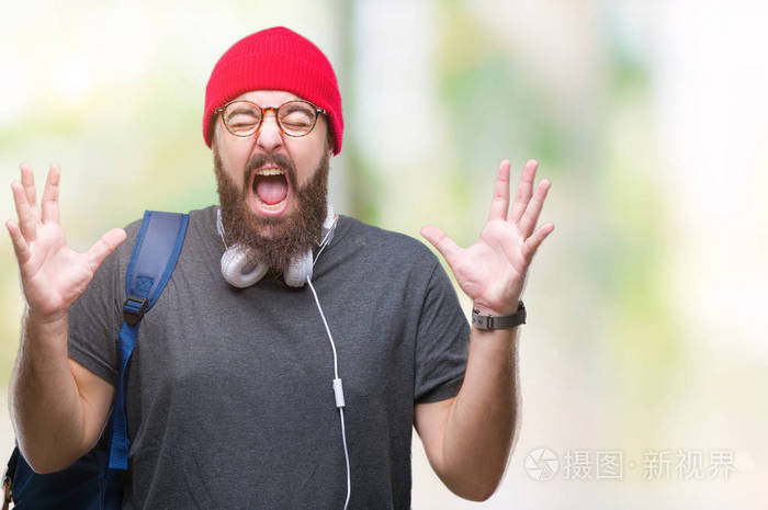 年轻的嬉皮士男子戴着红色羊毛帽和背包，在孤立的背景上庆祝疯狂和疯狂的成功，手臂抬起和闭上的眼睛尖叫兴奋。 赢家概念