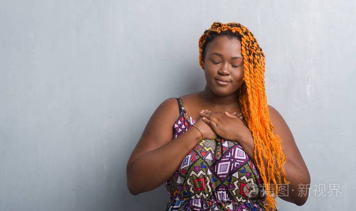年轻的非洲裔美国妇女在灰色的格朗格墙上,戴着橙色的辫子,双手胸部