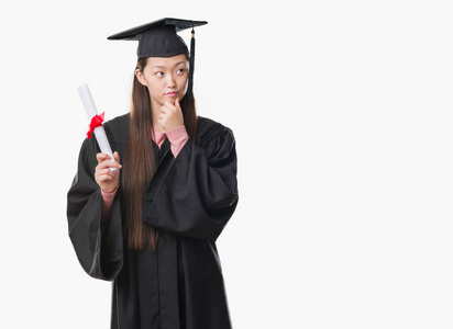 年轻的中国妇女穿着研究生制服拿着纸学位认真面对思考问题很困惑的想法