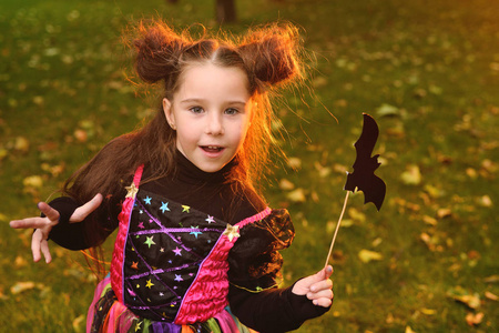 小女孩在嘉年华服装和魔术棒与蝙蝠