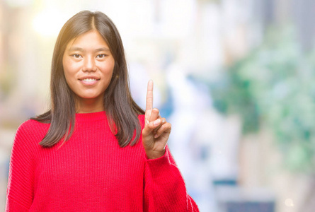 年轻的亚洲女人穿着冬天的毛衣，在孤立的背景上显示和指着第一个手指，同时微笑自信和快乐。