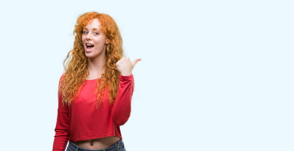 年轻的红发女人用拇指指着并向旁边展示，脸上洋溢着幸福的笑容