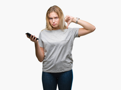 年轻的白种人女人用智能手机在孤立的背景下发送信息，愤怒的脸，负面的迹象，显示不喜欢，拇指向下拒绝的概念