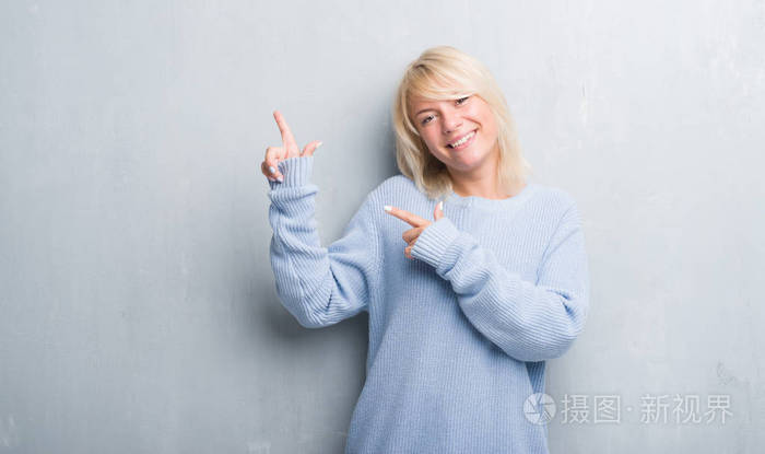 着冬天的毛衣,穿着灰色的墙壁,微笑着看着镜头,两只手和手指指向一边