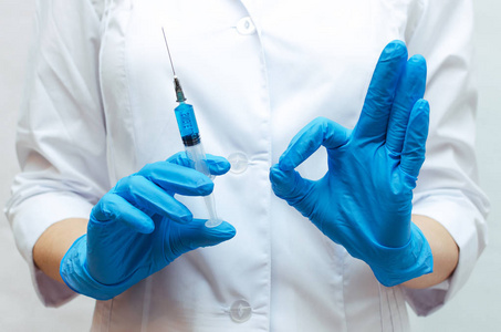 带蓝色药物的注射器和医生的手显示一个好的标志。