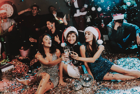 三位年轻妇女庆祝新年。圣诞老人帽。红帽里的人。新年快乐理念。一杯香槟。庆祝新年理念。穿裙子的年轻女人。