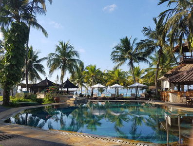 游泳池和酒吧设施周围的棕榈树，在印度尼西亚巴厘岛的一个念达萨海滩度假，为旅行背景。