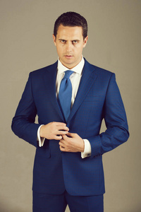 英俊的男人自信的商人或成功的老板与时尚的头发理发按钮在优雅的蓝色正式西装夹克灰色背景。 商业时尚和成功。 着装规范