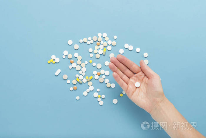 雌性手拿着一颗药丸在手掌上的蓝色背景上,上面有散落的药丸.