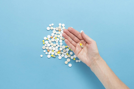 雌性手拿着一颗药丸在手掌上的蓝色背景上,上面有散落的药丸.