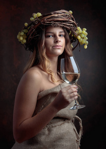 年轻漂亮的女人带着一杯白葡萄酒。 头上有葡萄的藤蔓花环。 美丽的女孩留着长发，完美的化妆。