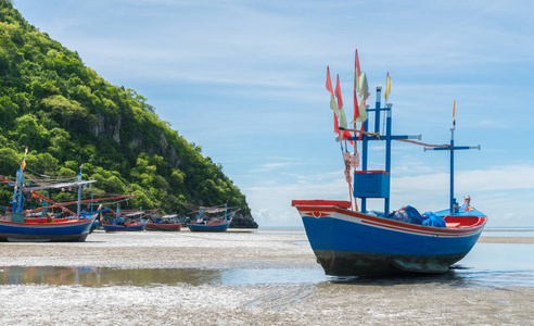蓝色渔船在海沙上与青山和其他渔民船在KhaoKalok海滩泰国。 渔人的船在灰沙中与树