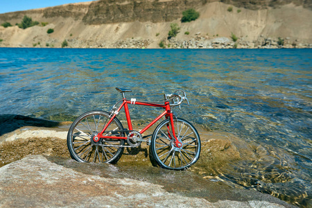 夏天晴朗的晴天，带着清澈的水在湖面上骑红色的金属玩具自行车