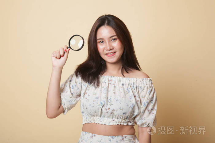 带着米色背景放大镜的年轻亚洲女人照片-正版商用图片13jdag-摄图新