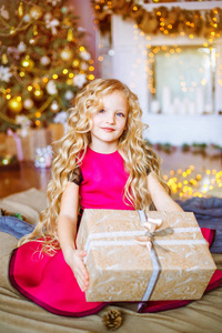 可爱的小女孩，长着长长的金发，在家附近的圣诞树上，有礼物花环和装饰的壁炉