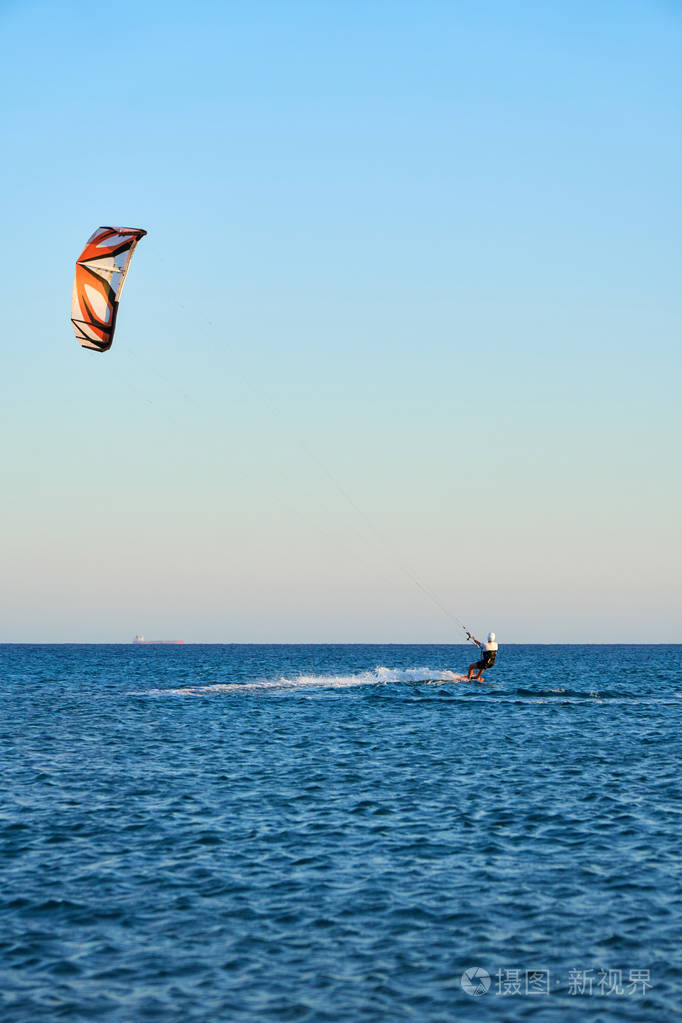 Kitesurfer在一艘漂浮的驳船的背景下迅速地在波浪上滑动
