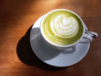 一杯热的抹茶绿茶拿铁或日本绿茶加一些牛奶，放在棕色的木桌上。在自然光线下感觉宁静