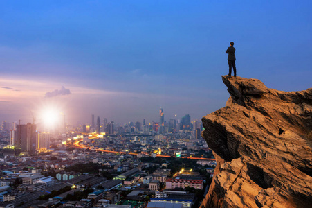 概念视觉商人穿着舒适的休闲服站在山顶,展望未来,与城市景观背景成功