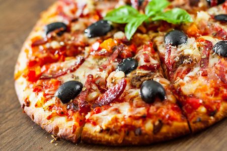 披萨片与莫扎雷拉奶酪，萨拉米，胡椒，火腿，意大利香肠，橄榄，香料和新鲜罗勒。 木制背景意大利披萨