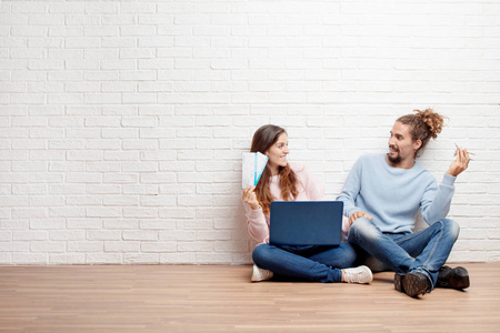 幸福的年轻夫妇坐在他们新房子的地板上，手提电脑买了一张登机票。 旅行概念。