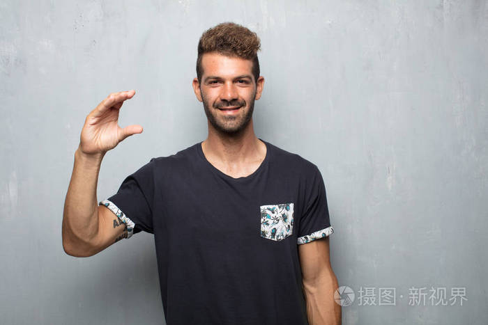 年轻的帅哥微笑着满意的表情显示出一个小物体或概念用一只手握着它